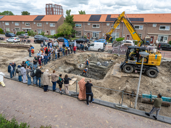 Geïnteresseerde mensen uit de buurt staan van achter hekken te kijken naar de opgravingsput.